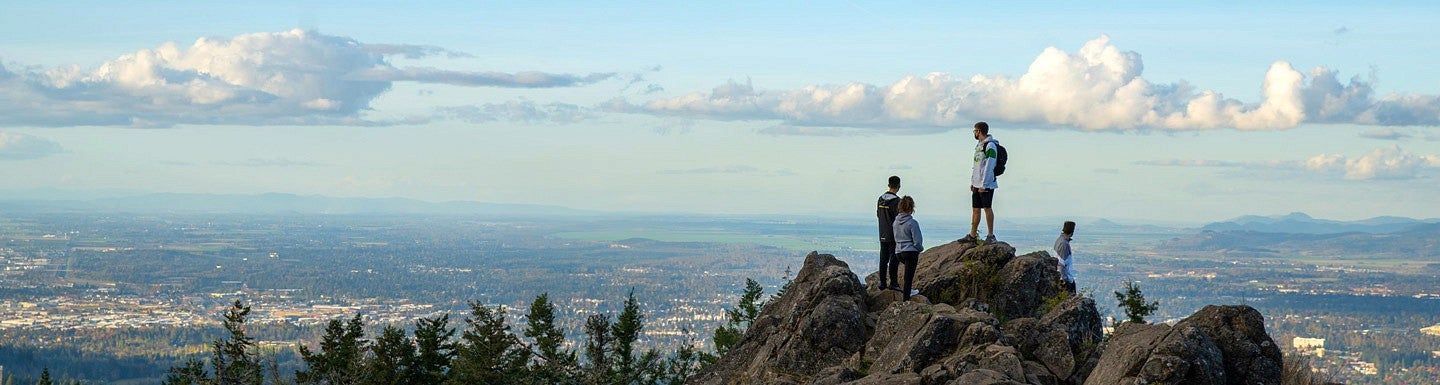 Hikers stand on the top of Spencer Butte looking out at the valley and clouds